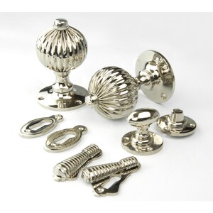 May include: A set of polished nickel door knobs with a fluted design. The set includes two knobs, two escutcheons, two keyhole covers, and two spindle covers.
