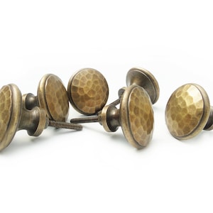 May include: Six antique brass cabinet knobs with a hammered finish. The knobs are round and have a slightly raised edge.