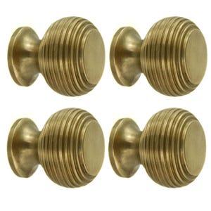 May include: Four antique brass cabinet knobs. Each knob features a round, ribbed design with a flat, circular face. The knobs are mounted on a small, flared base. The hardware is a warm, golden colour.