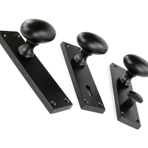 May include: Three black door handle sets with oval knobs and rectangular or triangular backplates. The hardware is made of metal and is set against a white background. The door handles are for interior doors.