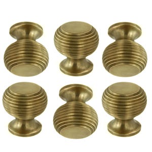 May include: Six antique brass cabinet knobs. Each knob features a round, ribbed body and a short, flared base. The knobs are a warm, golden colour and are arranged in two rows of three.