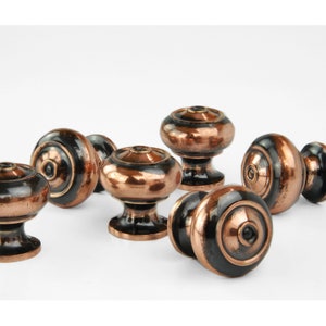 May include: A set of six copper and black cabinet knobs with a rounded, domed shape. The knobs have a distressed finish, giving them a vintage look.