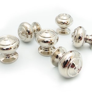 May include: Six polished nickel cabinet knobs with a round, slightly domed shape and a raised, concentric ring design.