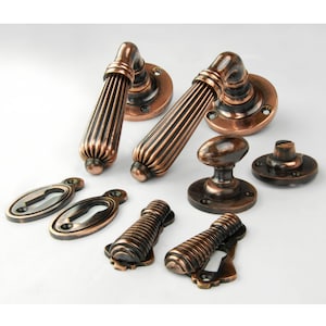 May include: A set of antique bronze door hardware, including two lever handles, a doorknob, a thumb turn, keyhole covers, and smaller handles. The hardware has a ribbed design and a warm, aged finish.