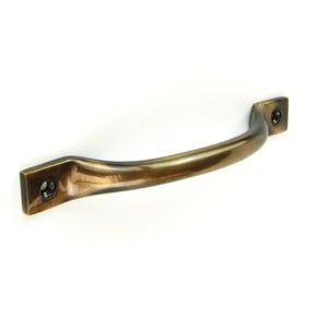 Op de afbeelding: Een bronzen kastgreep met een gebogen stang en vierkante montageplaten. De greep heeft een gladde, gepolijste afwerking en twee schroefgaten aan elk uiteinde voor installatie. De hardware is ontworpen voor meubels of kasten.