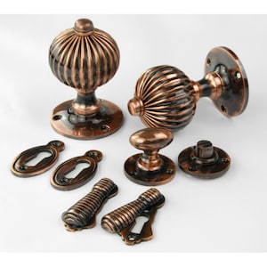 May include: Set of antique copper door knobs with a ribbed design. The set includes two door knobs, two escutcheons, two keyhole covers, and two rosettes.