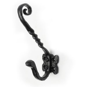 May include: Black metal coat hook with a twisted design and a decorative scroll at the top. The hook is mounted on a wall.