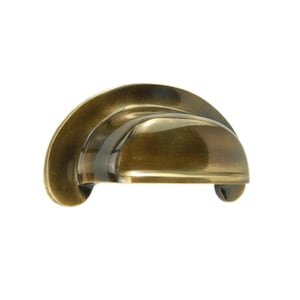 Op de afbeelding: Een bronskleurige, halvemaanvormige kastgreep met een gebogen ontwerp. De greep heeft een gladde, gepolijste afwerking en twee kleine, afgeronde voetjes. Geschikt voor laden en kasten.