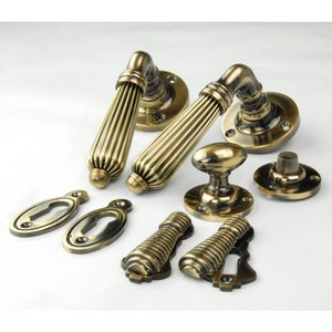 May include: A set of antique brass door hardware, including two door handles, two keyhole escutcheons, two door knobs, and two decorative escutcheons. The handles have a fluted design and the knobs are oval shaped.