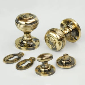 May include: A set of antique brass door knobs with keyhole escutcheons and a latch. The knobs have a decorative, grooved design.