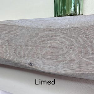 May include: Close-up of a limed wooden shelf with visible wood grain. The shelf is a light gray color and has a slightly curved shape. The word "Limed" is printed in black text at the bottom of the image. A green glass object sits on the shelf.