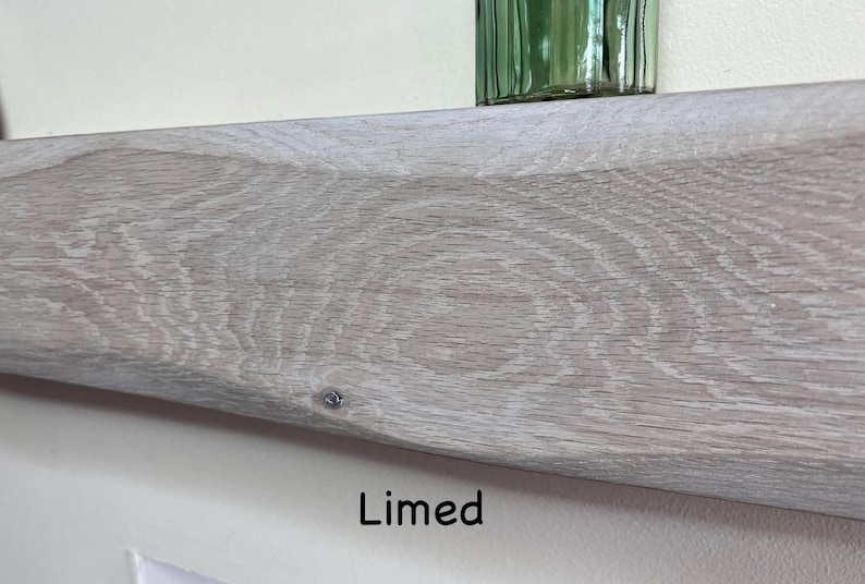 May include: Close-up of a limed wooden shelf with visible wood grain. The shelf is a light gray color and has a slightly curved shape. The word "Limed" is printed in black text at the bottom of the image. A green glass object sits on the shelf.