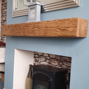 May include: A light blue wall with a wooden mantel shelf above a black electric fireplace. The mantel shelf has a white clock on it. The fireplace has a brown vase next to it.