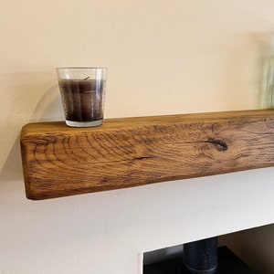 May include: A rustic wooden mantel shelf with a clear glass candle holder and a green glass bottle with a brown ribbon on top.