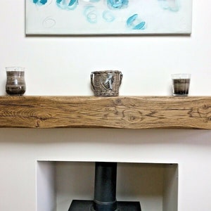 May include: A rustic wooden mantel shelf with a natural wood finish. The shelf is mounted above a fireplace and has two candles and a wicker basket on top.