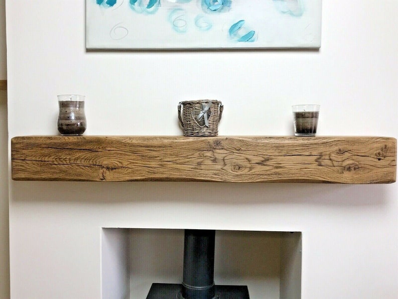 May include: A rustic wooden mantel shelf with a natural wood finish. The shelf is mounted above a fireplace and has two candles and a wicker basket on top.
