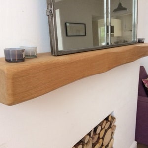 May include: A natural wood floating shelf with a live edge, mounted on a white wall. Two small glass candle holders sit on the shelf, and a rectangular mirror is mounted above. The shelf is approximately 60 inches long.