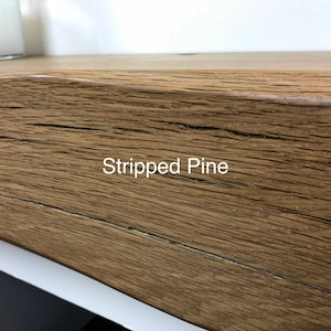 May include: Close-up of a section of a wooden shelf with the text "Stripped Pine" in white. The wood has a natural, textured grain and a warm, brown color. The shelf appears to be part of a larger piece of furniture.