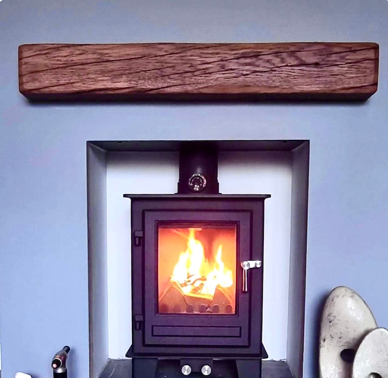 May include: A black wood-burning stove with a glass door and a fire burning inside. The stove is set into a fireplace with a wooden mantel above it.