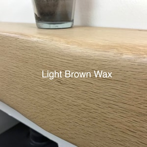 May include: Close-up of a light brown wooden shelf with a natural grain pattern. The text "Light Brown Wax" is visible on the shelf. A glass container sits on the shelf.