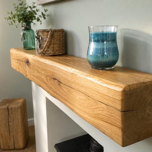 May include: A solid oak mantelpiece with a live edge, displaying a blue candle in a glass holder, a wicker basket, and a green glass vase with foliage. A small wooden block is positioned below.