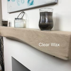 May include: A light-colored wooden shelf with a curved design, holding a candle in a glass jar, a small glass, and a larger candle in a glass. The text "Clear Wax" is printed on the shelf.