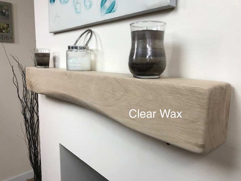 May include: A light-colored wooden shelf with a curved design, holding a candle in a glass jar, a small glass, and a larger candle in a glass. The text "Clear Wax" is printed on the shelf.