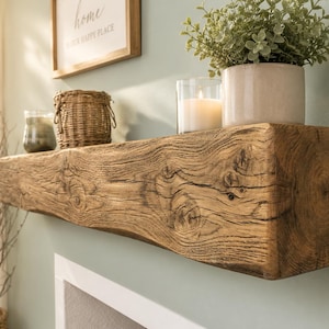 May include: A rustic wooden mantel shelf featuring a natural, weathered grain pattern with visible knots and a rough-hewn texture. The rectangular beam is mounted horizontally, showcasing a deep brown finish that highlights the organic wood rings.
