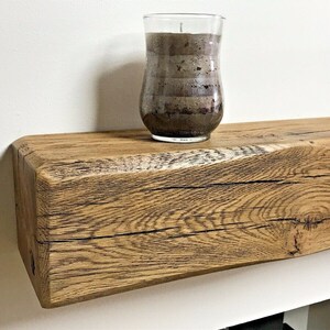 May include: A rustic wooden shelf with a natural wood finish. The shelf is made from reclaimed wood and has a unique, weathered look. A glass candle holder sits on the shelf.