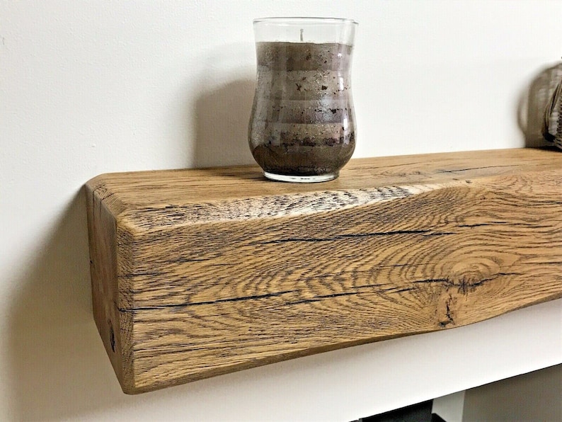 May include: A rustic wooden shelf with a natural wood finish. The shelf is made from reclaimed wood and has a unique, weathered look. A glass candle holder sits on the shelf.
