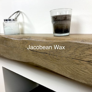 May include: A wooden mantel with a rough, textured surface. Two candles in glass containers and a jar candle with a metal handle are on the mantel. The text "Jacobean Wax" is visible on the mantel.