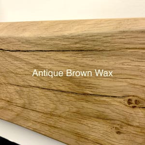 May include: Close-up of a section of a wooden beam with a light brown finish. The wood grain is visible, with a few cracks and knots. The text "Antique Brown Wax" is printed on the wood.
