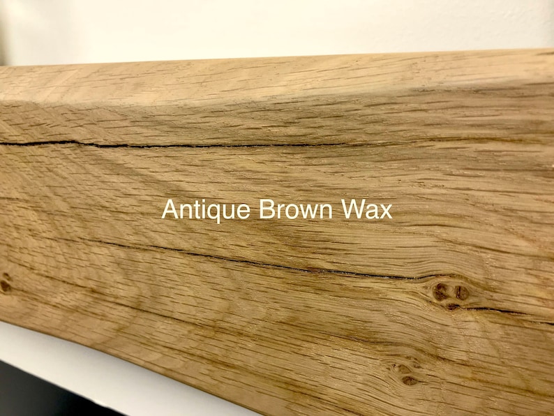 May include: Close-up of a section of a wooden beam with a light brown finish. The wood grain is visible, with a few cracks and knots. The text "Antique Brown Wax" is printed on the wood.