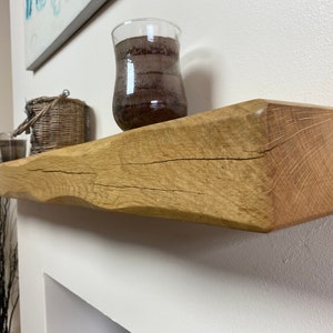 May include: A natural wood floating shelf with a live edge. The shelf is light brown with visible wood grain and a rough, textured surface. A decorative glass vase and a woven basket sit on the shelf, adding a rustic touch to the decor.