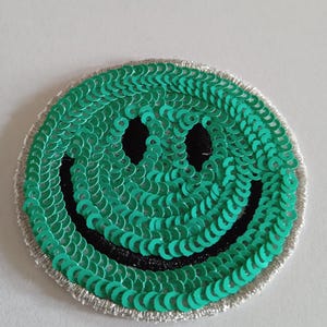 Peut inclure: Un patch smiley en sequins verts avec un contour noir et une bordure argentée.