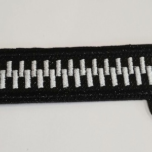 Peut inclure: Un patch brodé de fermeture éclair noir et blanc. La fermeture éclair est blanche et le fond est noir.