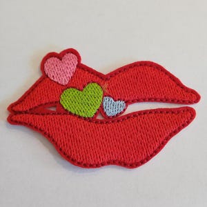 Peut inclure: Lèvres rouges brodées avec trois petits cœurs en rose, vert et bleu.