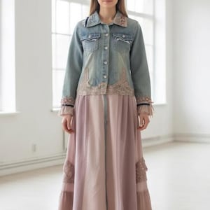 May include: A light blue denim jacket with floral embroidery and lace detailing is paired with a long, flowing pink skirt. The skirt features vertical panels of varying shades of pink and lace accents. The outfit is completed with nude heels.