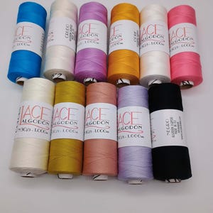 Może przedstawiać: Jedenaście szpulek nici Lace Algodón ułożonych w dwóch rzędach. Szpulki mają różne jednolite kolory, w tym niebieski, biały, fioletowy, żółty, różowy, kremowy, złoty, brzoskwiniowy, lawendowy i czarny. Każda szpulka ma białą etykietę z tekstem.