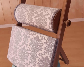 May include: A wooden stand with a padded roll and a padded seat, both covered in a white fabric with a gray floral pattern.
