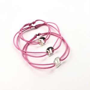 Puede incluir: Tres pulseras de amistad de color rosa con dijes plateados con las letras A, J y M.