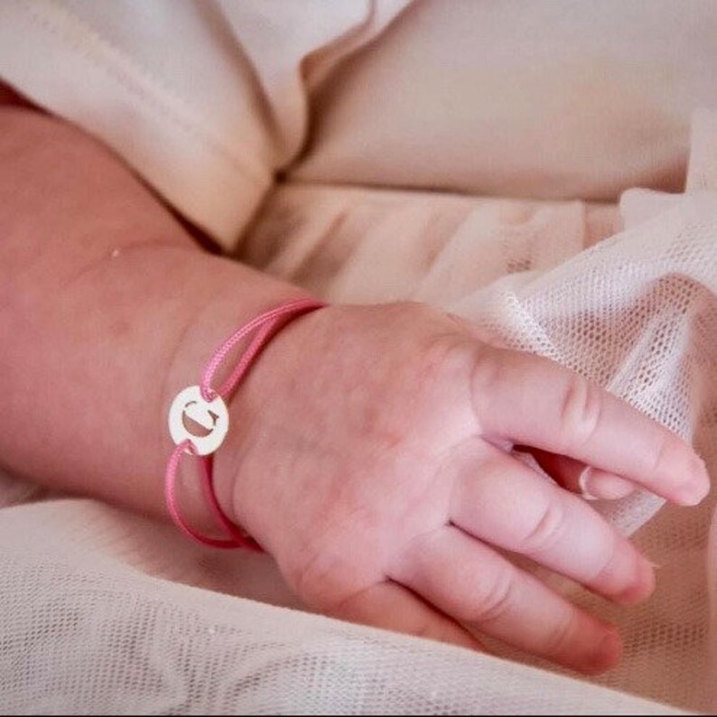 Puede incluir: Un brazalete de cord&oacute;n rosa con un dije de plata con la letra "G".