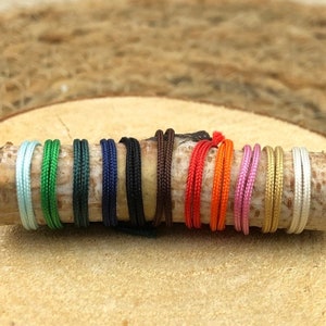 Puede incluir: Una colecci&oacute;n de 12 cordones de diferentes colores, dispuestos en una fila sobre una superficie de madera. Los cordones tienen todos el mismo grosor y est&aacute;n hechos de un material suave y liso.