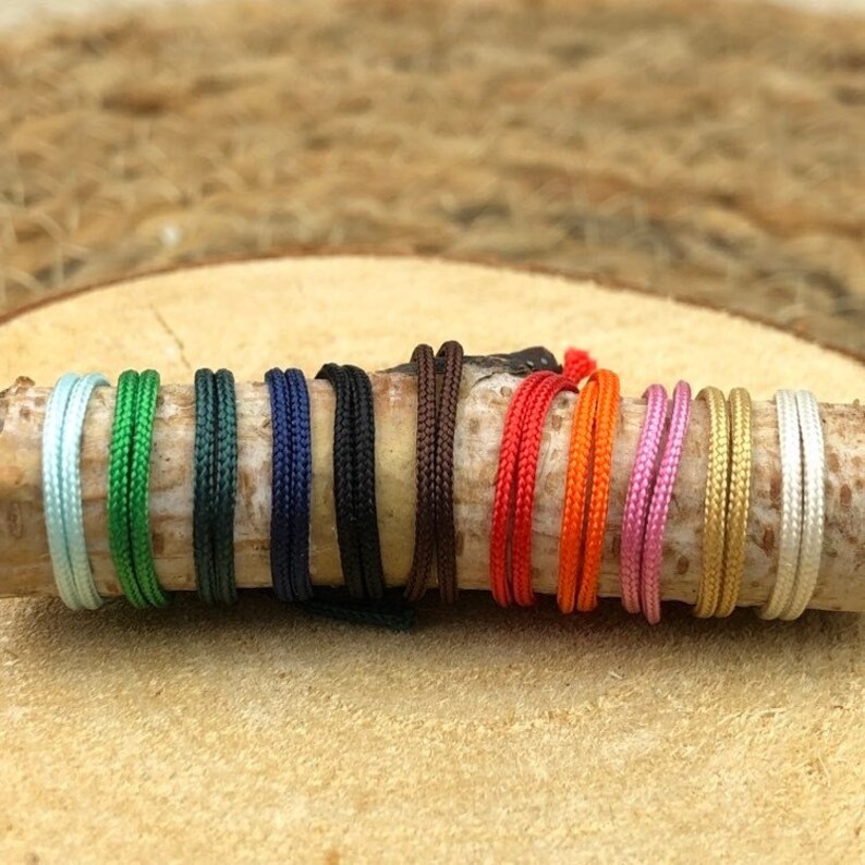 Puede incluir: Una colecci&oacute;n de 12 cordones de diferentes colores, dispuestos en una fila sobre una superficie de madera. Los cordones tienen todos el mismo grosor y est&aacute;n hechos de un material suave y liso.
