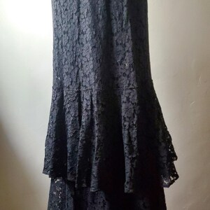 May include: A floor-length black lace dress with a tiered skirt. The dress has a fitted bodice and a flared skirt, creating an elegant silhouette. The intricate lace pattern adds texture and visual interest to the garment.