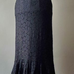 May include: A black lace dress displayed on a mannequin. The dress features a fitted bodice, a flared skirt with a ruffled hem, and a delicate lace overlay. The dress is floor-length and suitable for formal occasions.