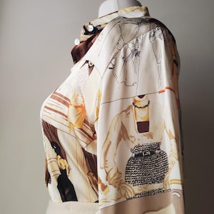 Puede incluir: Una camisa crema con botones con un estampado &uacute;nico que presenta ilustraciones de figuras en varias poses, en tonos marr&oacute;n, negro y amarillo. La camisa de manga larga se exhibe en un maniqu&iacute;.