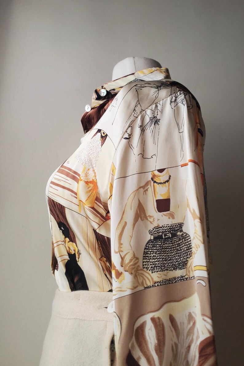 Puede incluir: Una camisa crema con botones con un estampado &uacute;nico que presenta ilustraciones de figuras en varias poses, en tonos marr&oacute;n, negro y amarillo. La camisa de manga larga se exhibe en un maniqu&iacute;.