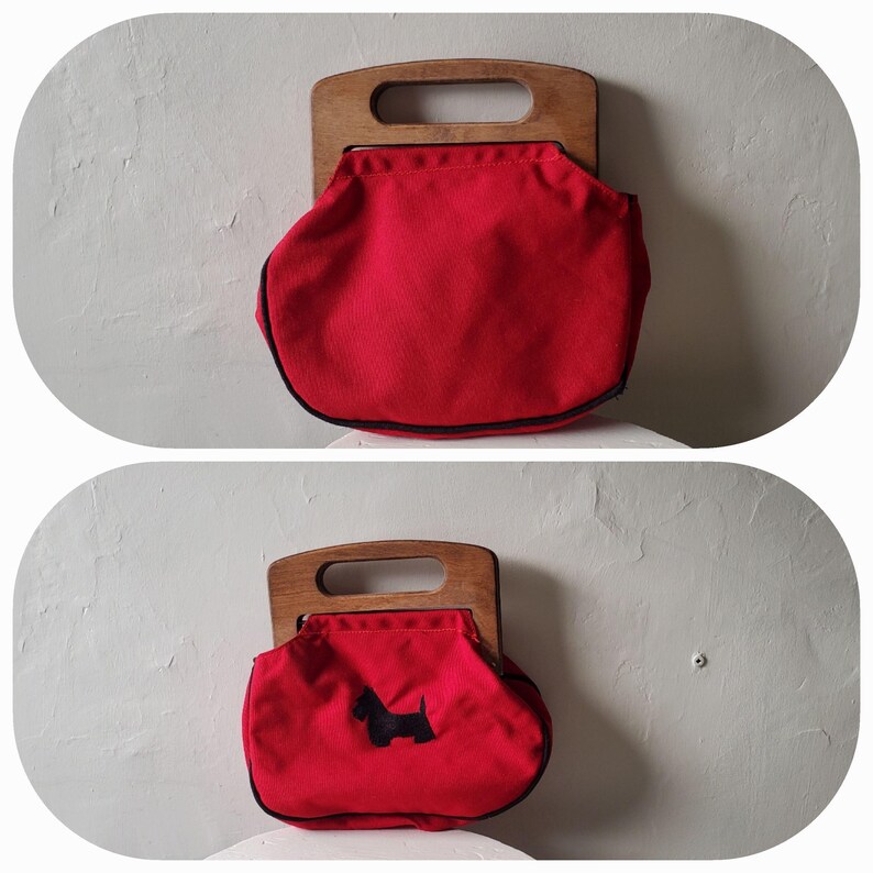 May include: A red handbag with a wooden handle. The bag has a black trim and a black silhouette of a dog on the front. The bag is a rounded shape and appears to be made of canvas or a similar material.