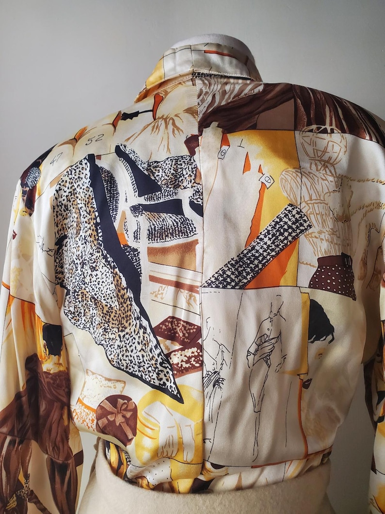 Puede incluir: Una blusa color crema con un dise&ntilde;o de patchwork &uacute;nico. La blusa presenta una variedad de patrones, incluyendo estampado de leopardo, formas geom&eacute;tricas y figuras esbozadas. La paleta de colores incluye crema, marr&oacute;n, negro y acentos naranja. La blusa tiene mangas largas y cuello.